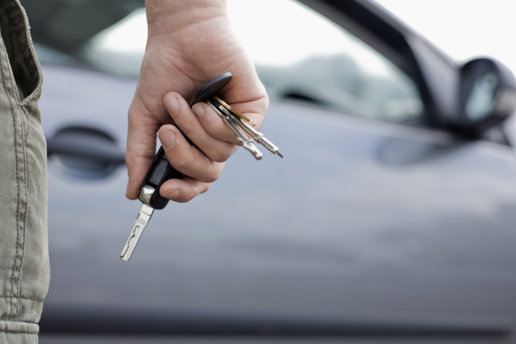 A customer holding keys near a car, deciding if he should lease or finance a vehicle 